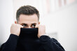 Close-up of a mysterious man partially hiding his face behind a black turtleneck