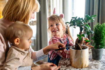 Wall Mural - Young woman with her children taking care of plants indoors. Family home gardening hobby concept.