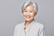 © Anna - A portrait of an Asian lady, a smiling elderly woman with gray hair, stands on a gray background. A place for text, a banner for advertising.