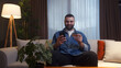 © mahirkart - Young adult man sitting on couch while enter credit card number on smartphone for makes secure easy distant electronic payment at home. Pay for goods services on internet, transactions, ecommerce