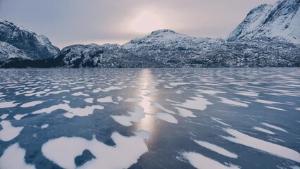 Wall Mural - Aerial view from low flying drone of frozen lake in snowy mountains in winter at sunrise. Lofoten islands, Norway. Top view of frosted river, reflection on ice, snowy rocks in fog, sky. Cloudy weather