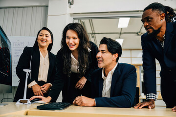 Wall Mural - Young professionals in a modern office embrace teamwork while working on a startup project. Three people analyze data on a computer, fostering discussion and leadership.