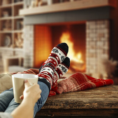 Wall Mural - Woman legs with warm winter socks. Home interior with fireplace and empty space for your decoration. Mockup background and december time. Cold winter and new year. 