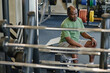 Elderly african american gym goer sitting on bench nearby exercise machines at fitness center