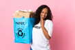 Teenager cuban girl holding a recycling bag full of paper to recycle isolated on pink background looking up while smiling