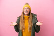 Young blonde woman wearing winter jacket isolated on pink background with shocked facial expression