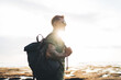 Happy man carrying backpack standing against ocean and sunlight
