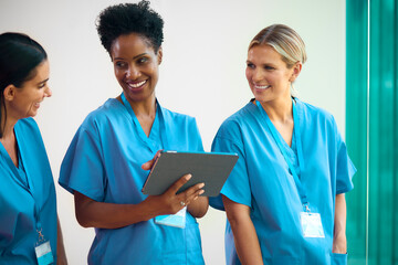 Team Of Mature Female Multi Cultural Medical Team In Scrubs With Digital Tablet Meeting In Hospital