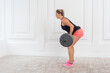 © khosrork - Side view portrait of athletic strong bodybuilder woman in pink shorts and black top doing exercises for gluteus muscle at gym with the barbell on white wall background. Indoor studio shot.