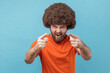 © khosrork - Portrait of angry man with Afro hairstyle wearing orange T-shirt pointing finger at camera choosing you, scolding and forcing to move on. Indoor studio shot isolated on blue background.