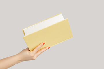 Closeup of woman hand holding open book or organizer. Indoor studio shot isolated on gray background.