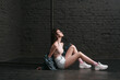 © khosrork - Full length side view portrait of beautiful woman with dark hair, sitting near fence on floor on dark brick wall background and looking up with concentrated expression. Indoor studio shot.