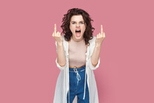 Portrait Of Rude Impolite Woman With Curly Hair Wearing Casual Style Outfit Standing Showing Middle Fingers, Screaming With Hate And Anger. Indoor Studio Shot Isolated On Pink Background.
