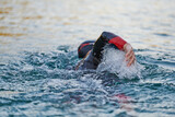 Fototapeta Sport - Triathlon athlete swimming on lake in sunrise wearing wetsuit