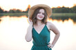 © Iryna - Portrait of happy cute smiling attractive traveler teenager girl wearing hat and green dress enjoy the relaxation and freedom. standing alone on pier with lake on background.