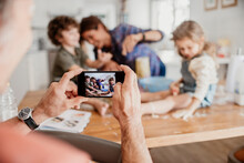 Father taking photo on smartphone of his wife and kids baking