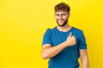 Wall Mural - Young handsome caucasian man isolated on yellow background giving a thumbs up gesture