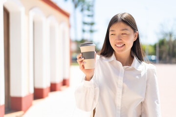 Wall Mural - Pretty Chinese woman holding a take away coffee at outdoors with happy expression