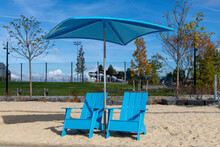 Two Blue Adirondack-style Chairs Under A Beach Umbrella On Gansevoort Beach, New York City, NY, USA Along The Hudson River Park On The Gansevoort Peninsula