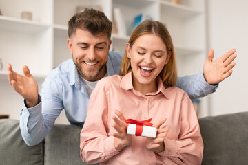 husband surprising wife giving wrapped present box to lady indoors