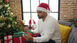 © Krakenimages.com - African american man using smartphone holding christmas gift at home