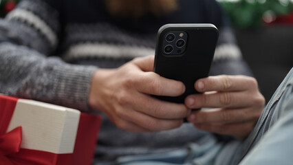 Sticker - Young redhead man using smartphone sitting on sofa by christmas decoration at home