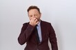 © Krakenimages.com - Middle age business man with beard wearing suit and tie smelling something stinky and disgusting, intolerable smell, holding breath with fingers on nose. bad smell
