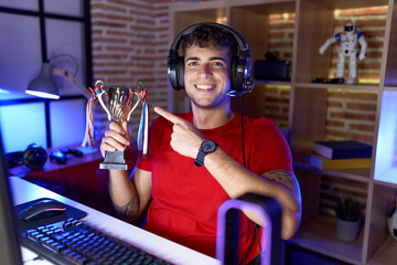 Sticker - Young hispanic man playing video games holding trophy smiling happy pointing with hand and finger