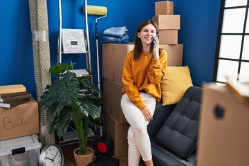 Poster - Young blonde woman talking on smartphone sitting on sofa at new home