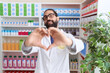 © Krakenimages.com - Hispanic man with beard working at pharmacy drugstore smiling in love showing heart symbol and shape with hands. romantic concept.