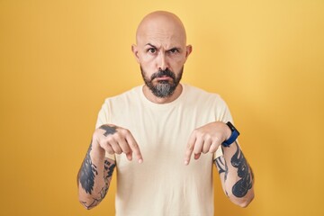 Wall Mural - Hispanic man with tattoos standing over yellow background pointing down looking sad and upset, indicating direction with fingers, unhappy and depressed.