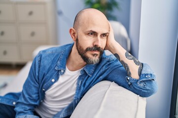 Canvas Print - Young bald man sitting on sofa with serious expression at home