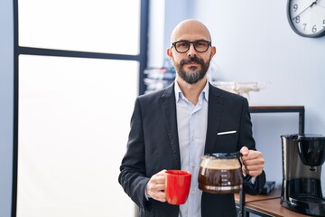 Canvas Print - Young bald man business worker holding cup and jar of coffee at office