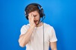 Hispanic man with beard listening to music wearing headphones yawning tired covering half face, eye and mouth with hand. face hurts in pain.