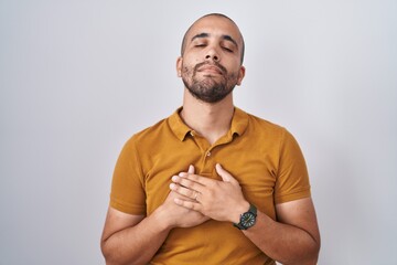 Poster - Hispanic man with beard standing over white background smiling with hands on chest with closed eyes and grateful gesture on face. health concept.