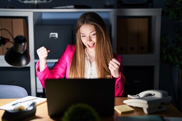 Canvas Print - Young caucasian woman working at the office at night very happy and excited doing winner gesture with arms raised, smiling and screaming for success. celebration concept.