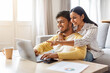 © Prostock-studio - Happy young indian couple websurfing on laptop together at home