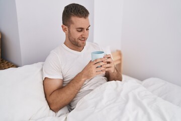 Sticker - Young caucasian man drinking cup of coffee sitting on bed at bedroom