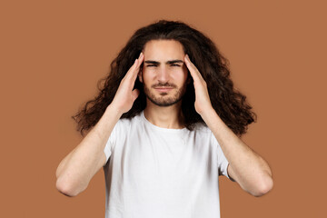 Hispanic guy touching temples suffering from headache against beige backdrop