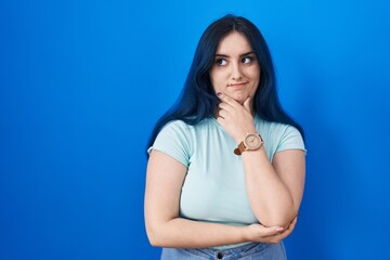 Poster - Young modern girl with blue hair standing over blue background thinking worried about a question, concerned and nervous with hand on chin