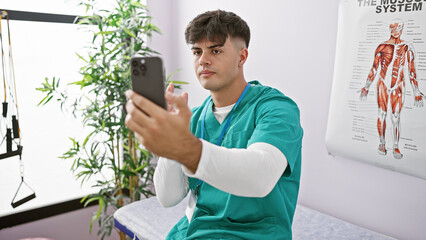 Canvas Print - Attractive young hispanic man working as physiotherapist in rehab clinic, engaging in serious video call on smartphone about patient's recovery journey