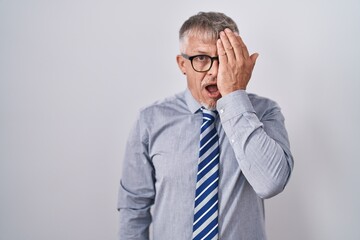 Wall Mural - Hispanic business man with grey hair wearing glasses covering one eye with hand, confident smile on face and surprise emotion.