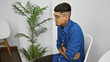 © Krakenimages.com - Suffering from stomachache, young hispanic man in business attire, tattooed and glasses-clad, sits in chair, nervous and in pain, awaiting interview in waiting room
