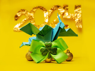 Blue paper origami dragon on golden balls and green ribbon with Irish shamrock, golden sign 2024 on yellow background. Year of powerful creature in Ireland. Hand made craft. Chinese horoscope.