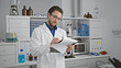 Young hispanic man scientist writing report standing at laboratory