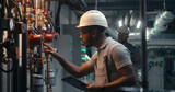 Fototapeta  - Male technician worker wearing safety uniform and hard hat works using tablet computer. African American inspector checks pipeline system on modern factory, plant or industrial energy facility.