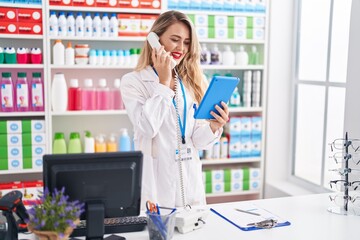 Wall Mural - Young beautiful hispanic woman pharmacist using touchpad talking on telephone at pharmacy