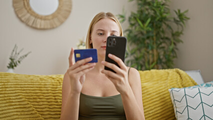 Wall Mural - Young blonde woman shopping with smartphone and credit card sitting on sofa at home