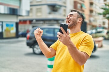 Sticker - Young hispanic man using smartphone with winner expression at street