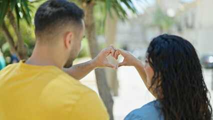 Wall Mural - Man and woman couple doing heart gesture standing backwards at park